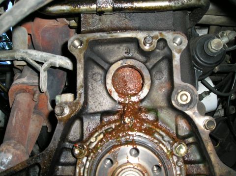 1986 Toyota Hilux - This engine block shows signs of a substantial oil leak, with fluid seeping from around a seal and onto the surrounding metal parts.