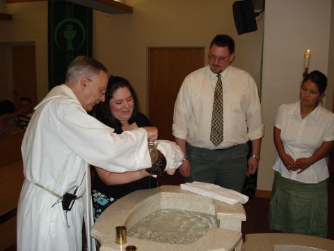 2000 Ford Crown Victoria - A baptism ceremony is taking place with a priest, parents, and a baby at the font.