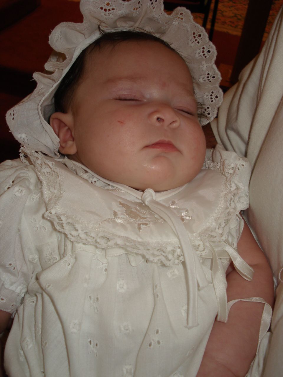 Baby sleeping in a white christening gown and bonnet