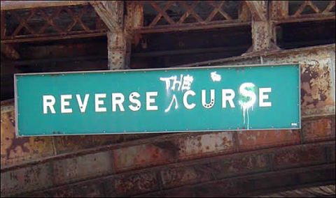 2005 Ford Excursion - A teal sign reading 'THE REVERSE CURSE' is mounted beneath a weathered, rusty bridge structure.