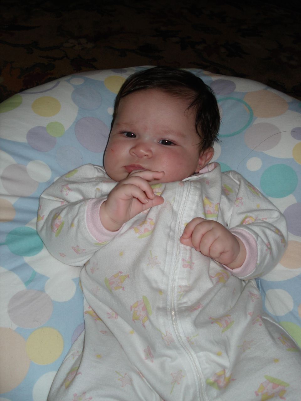 Baby in a white sleeper with pink trim, lying on a patterned pillow