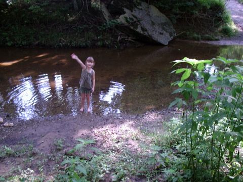 1996 Ford Bronco - A young child stands in a creek bed, waving to the camera amidst natural surroundings.