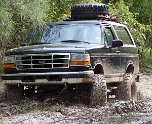 1986 Ford Bronco - This Ford Bronco is navigating a muddy trail with a spare tire mounted on its roof rack.