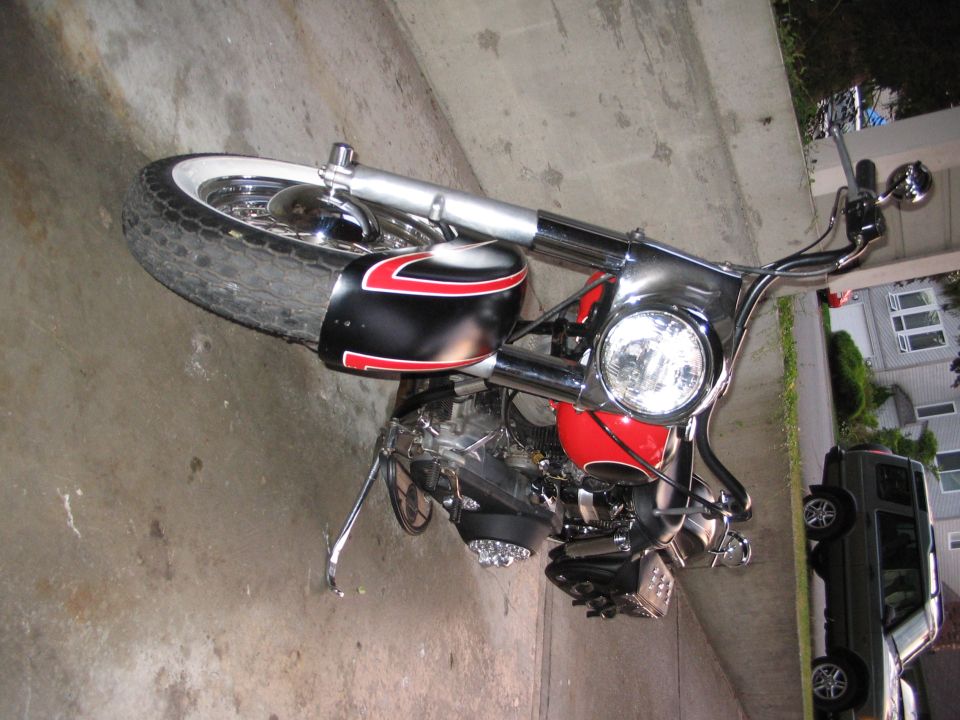 Red and black bobber motorcycle with pinstriped fender and chrome headlight parked in a driveway