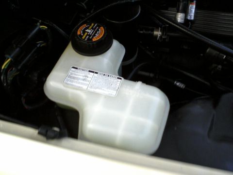 1996 Mercury Grand Marquis - Close-up of a white plastic coolant reservoir with warning labels and a black cap in an engine bay.