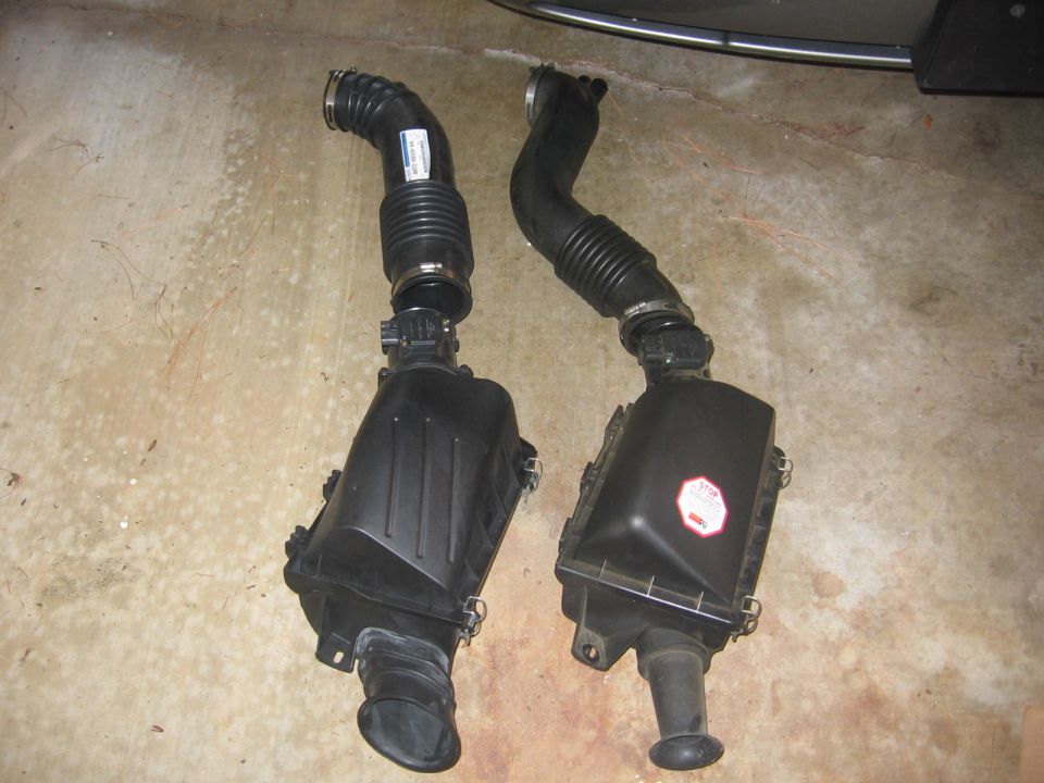 Two black airbox assemblies with intake hoses on a concrete garage floor
