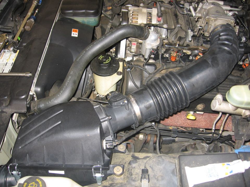 Engine bay with air intake system and hoses visible. Some engine components are also in view