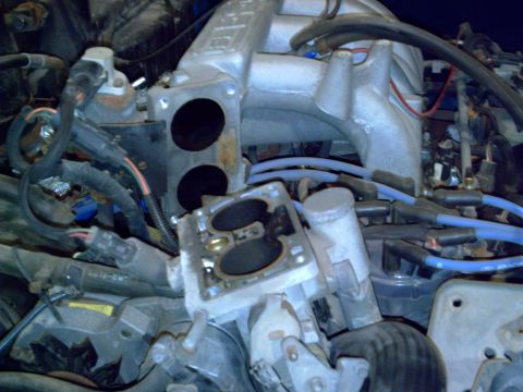 1990 Ford Bronco - Close-up view of a vehicle's engine components, focusing on the throttle body and intake manifold.