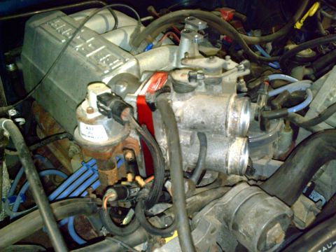 1990 Ford Bronco - Close-up view of an engine's throttle body assembly, a red stripe and a visible part number label.