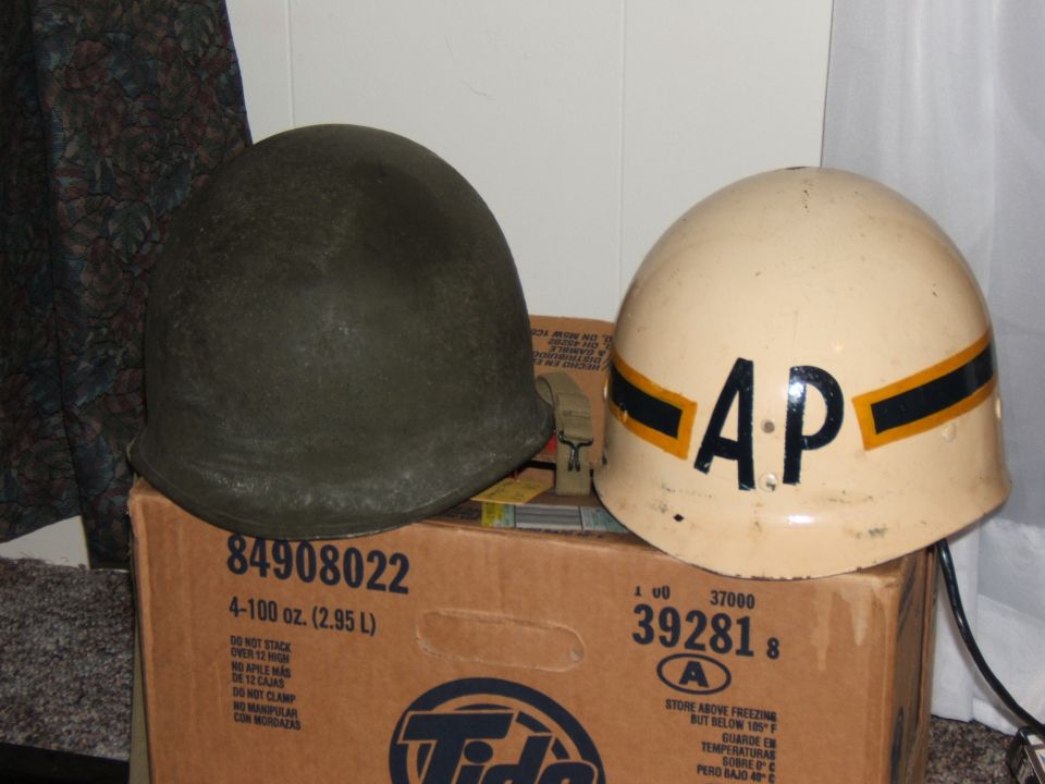 Two military helmets, one green and one cream with AP marking