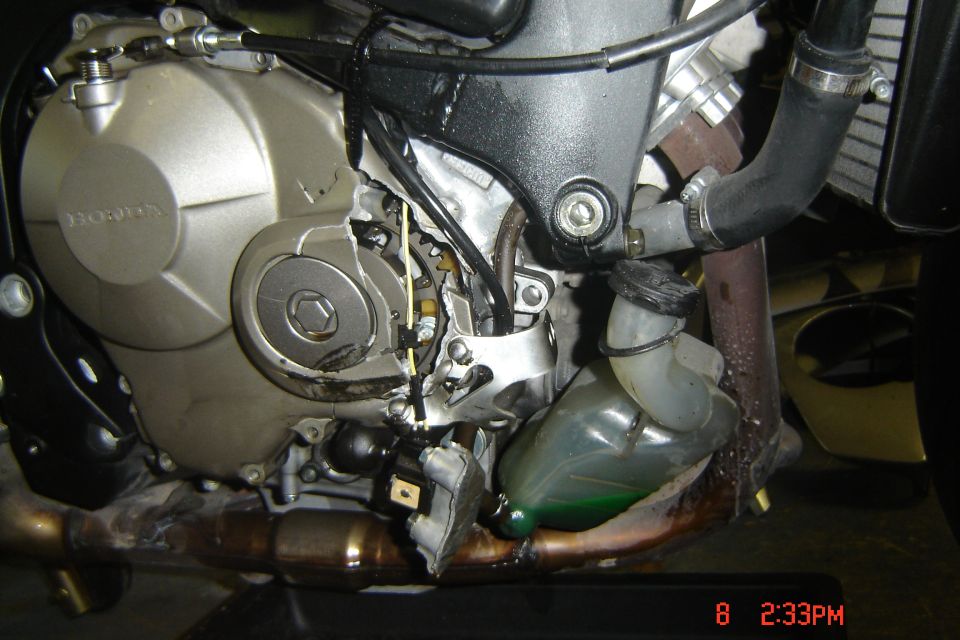 Close-up of a damaged motorcycle engine, showing broken casing and exposed wires