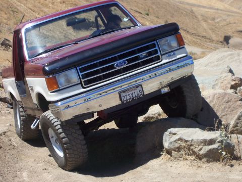 1991 Ford Bronco - A maroon and white Ford F-Series truck navigates a rocky terrain.