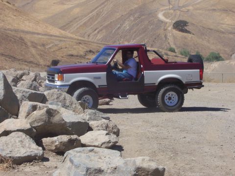 1991 Ford Bronco - Two-tone red and white 1991 Ford Bronco with spare tire on back, parked off-road.