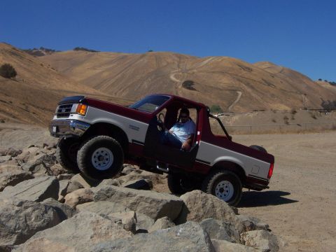 1991 Ford Bronco - A red and white 1991 Ford Bronco navigates a rocky terrain under a clear blue sky.
