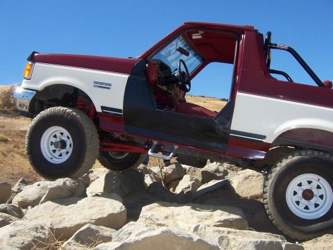 1991 Ford Bronco - A modified 1991 Ford Bronco navigates a rocky terrain with its doors off.