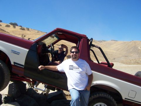 1991 Ford Bronco - A red and white 1991 Ford Bronco is shown off-road with two men posing near the vehicle.
