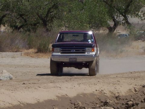 1991 Ford Bronco - A maroon and white 1991 Ford Bronco kicks up dust as it drives down a dirt road.