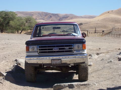 1991 Ford Bronco - This Ford F-Series truck is parked in a dry, hilly area with some trees and a fence visible.