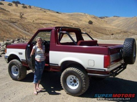 1991 Ford Bronco - A woman stands next to a two-tone Ford Bronco in a dry, hilly landscape.