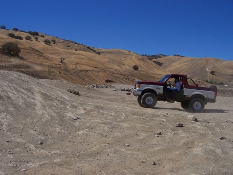 1991 Ford Bronco - A 1991 Ford Bronco navigates a dirt path in a dry, hilly landscape under a clear blue sky.