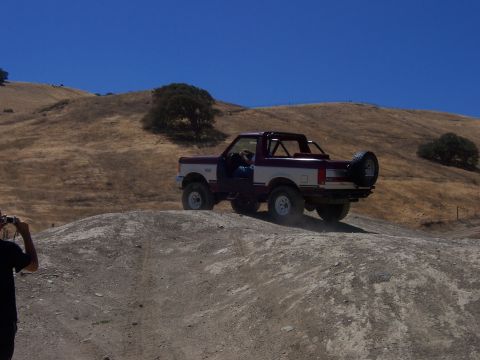 1991 Ford Bronco - A two-tone Ford Bronco navigates a dusty, off-road terrain under a clear blue sky.