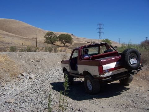 1991 Ford Bronco - A 1991 Ford Bronco is seen off-road on a sunny day with a dry, hilly landscape.