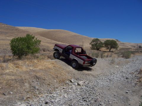 1991 Ford Bronco - A red and white 1991 Ford Bronco navigates an off-road trail on a sunny day.