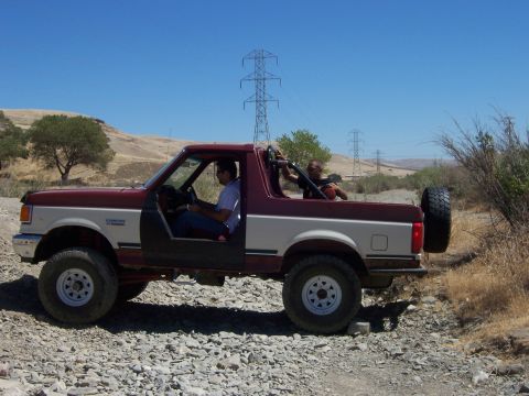 1991 Ford Bronco - Two men are on a dirt road in a modified Ford Bronco with the doors off.