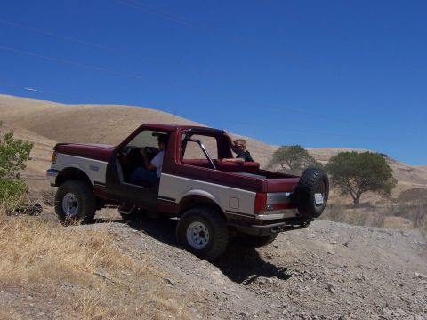 1991 Ford Bronco - A red and beige 1991 Ford Bronco is shown off-roading with two occupants.
