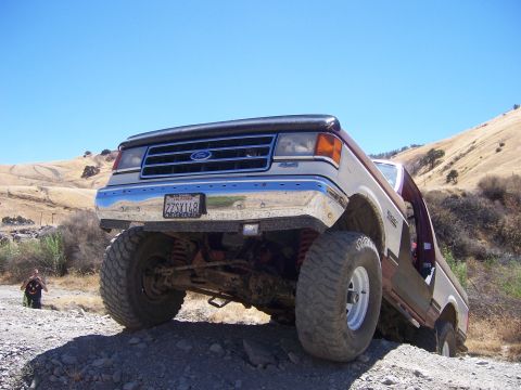1991 Ford Bronco - This modified Ford Bronco is navigating a steep, rocky trail under a clear blue sky.