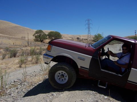 1991 Ford Bronco - A man drives a red and white 1991 Ford Bronco off-road on a sunny day.