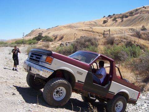 1991 Ford Bronco - A two-tone Ford Bronco navigates a rocky incline on a sunny day.