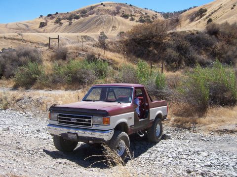 1991 Ford Bronco - Maroon and white 1991 Ford Bronco parked off-road on a gravelly surface.