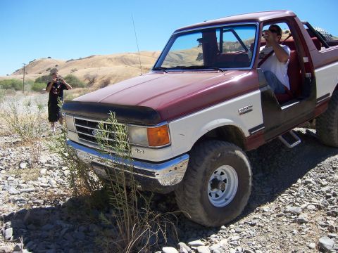 1991 Ford Bronco - A two-tone Ford Bronco is parked on a rocky surface under a clear blue sky.