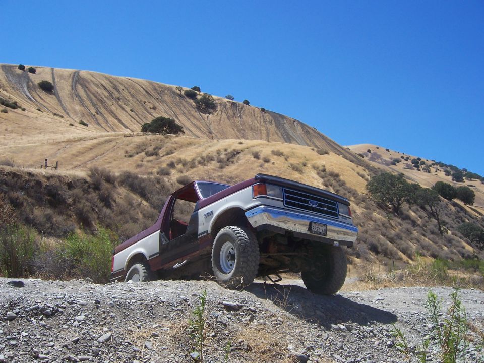 1991 Ford Bronco with a two-tone maroon and white paint job, driving off-road on a gravel path