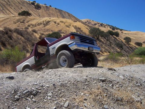 1991 Ford Bronco - A two-tone 1991 Ford Bronco, with its doors removed, tackles a challenging rocky terrain on a sunny day.