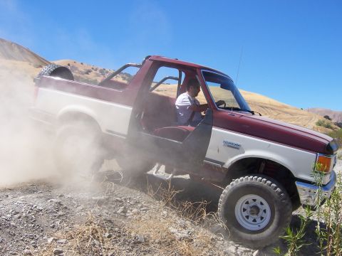 1991 Ford Bronco - Ford Bronco kicks up dust while navigating a dry, hilly terrain.