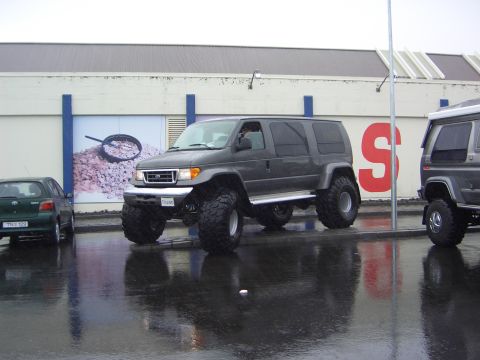 1996 Ford Bronco - A lifted van with large tires is parked next to a smaller car and another van.