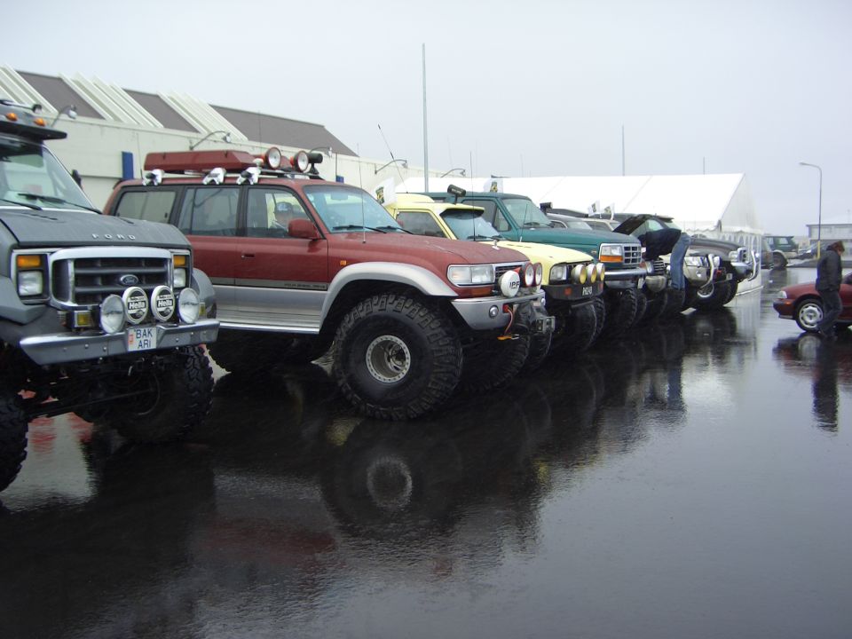 Row of lifted 4x4 trucks on big tires on a wet lot under gray skies