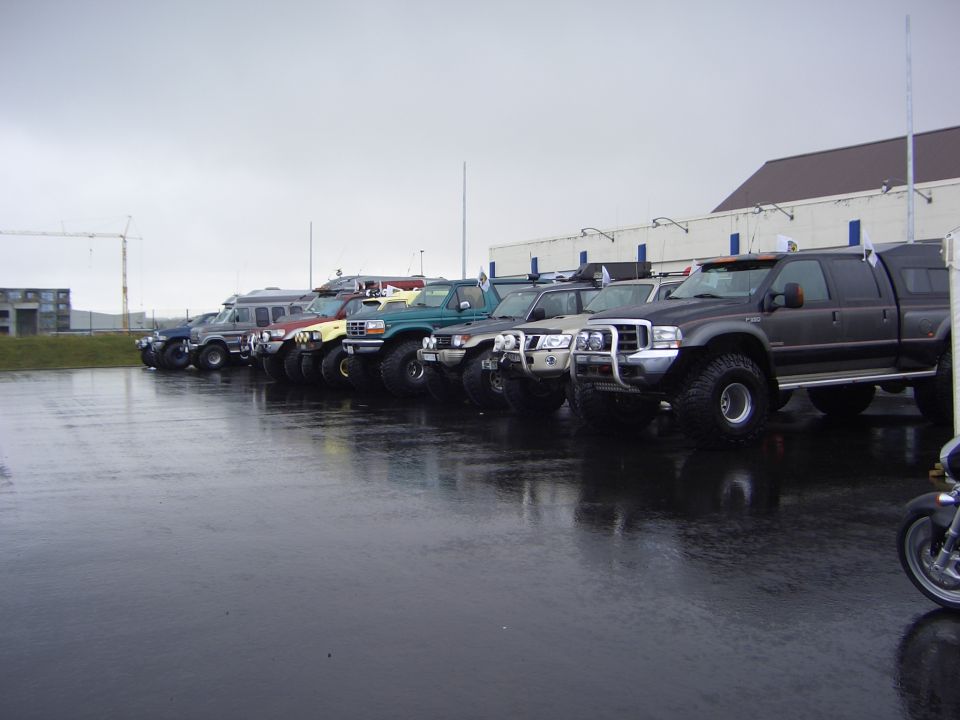 Row of lifted 4x4 trucks and SUVs on big tires parked on a wet lot.