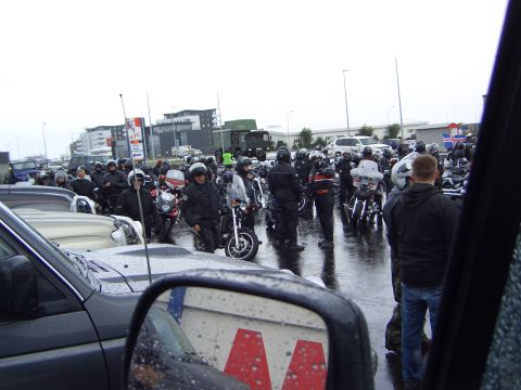 1996 Ford Bronco - A large group of motorcyclists are gathered in a wet parking lot, with buildings and a KFC sign in the background.