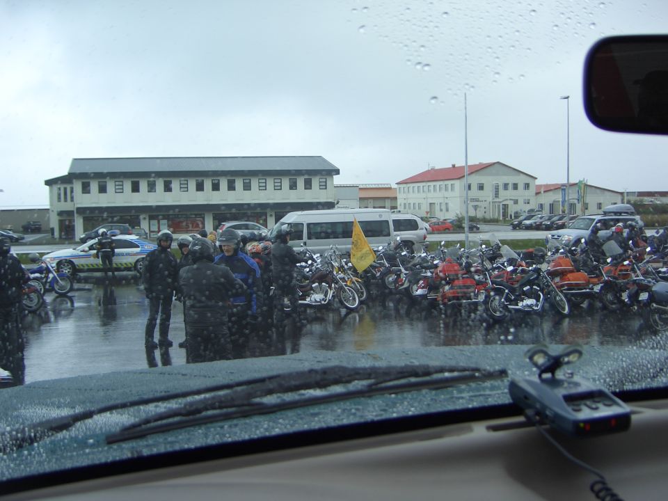 Rainy parking lot full of motorcycles and riders seen through a car windshield