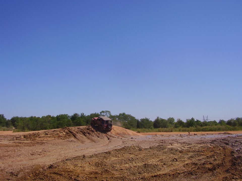 Off-road vehicle climbing a dirt mound under a clear blue sky