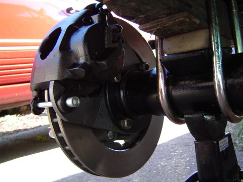 1978 Ford Bronco - Close-up view of a vehicle's brake caliper and rotor assembly, with a red vehicle in the background.