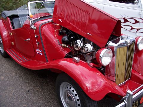 1972 Ford Ranchero - A red convertible with its hood open, revealing the engine and a Union Jack emblem on the door, parked next to another vehicle.