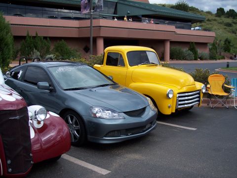 1972 Ford Ranchero - A bright yellow pickup truck and a modern gray coupe are parked side-by-side in a lot.