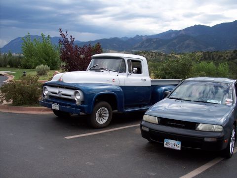 1972 Ford Ranchero - A classic Ford F-100 pickup truck is parked next to a modern sedan with mountains in the background.