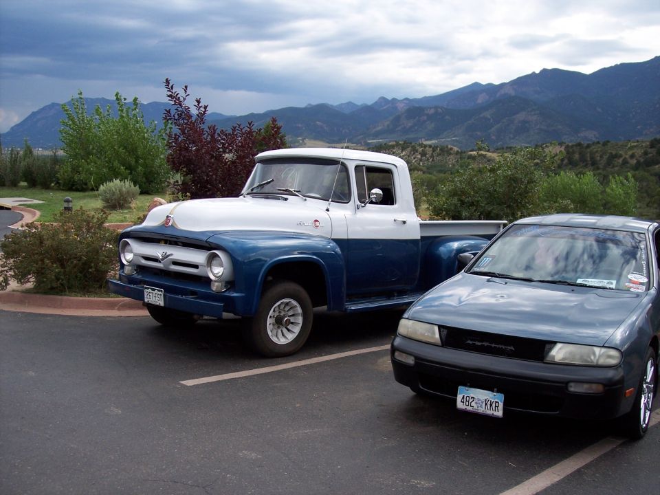 Two-tone blue and white 1956 Ford F-100 pickup truck parked next to a dark sedan