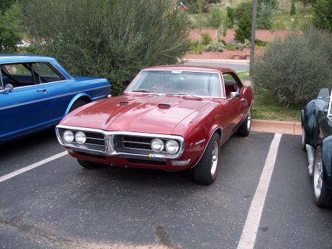 1972 Ford Ranchero - A red coupe with dual hood scoops and a chrome grille is parked in a lot next to other vehicles.