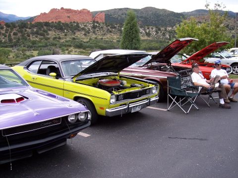 1972 Ford Ranchero - A row of classic cars, including a yellow muscle car and a purple Challenger, are displayed at a car show with a scenic mountain backdrop.